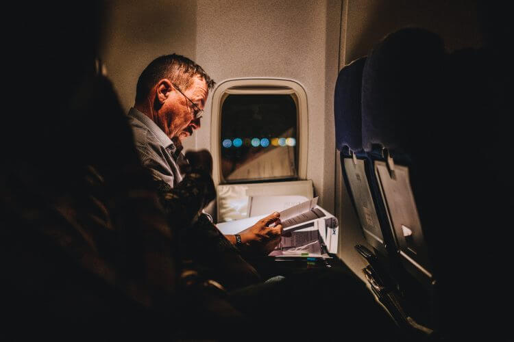 In this image, a person is seen reading a book during a long flight