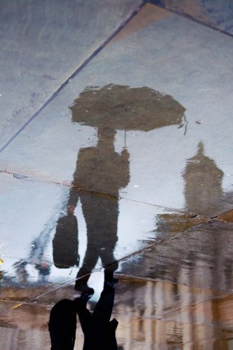 A reflection of a person carrying a windproof umbrella is seen here