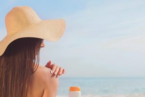 Woman on beach wearing hat applying suncream
