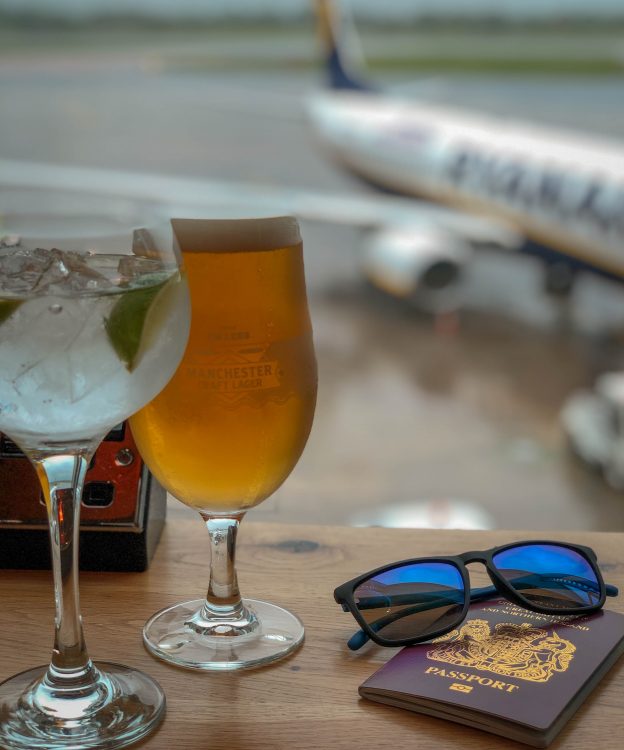 Two drinks and a passport in front of an airplane